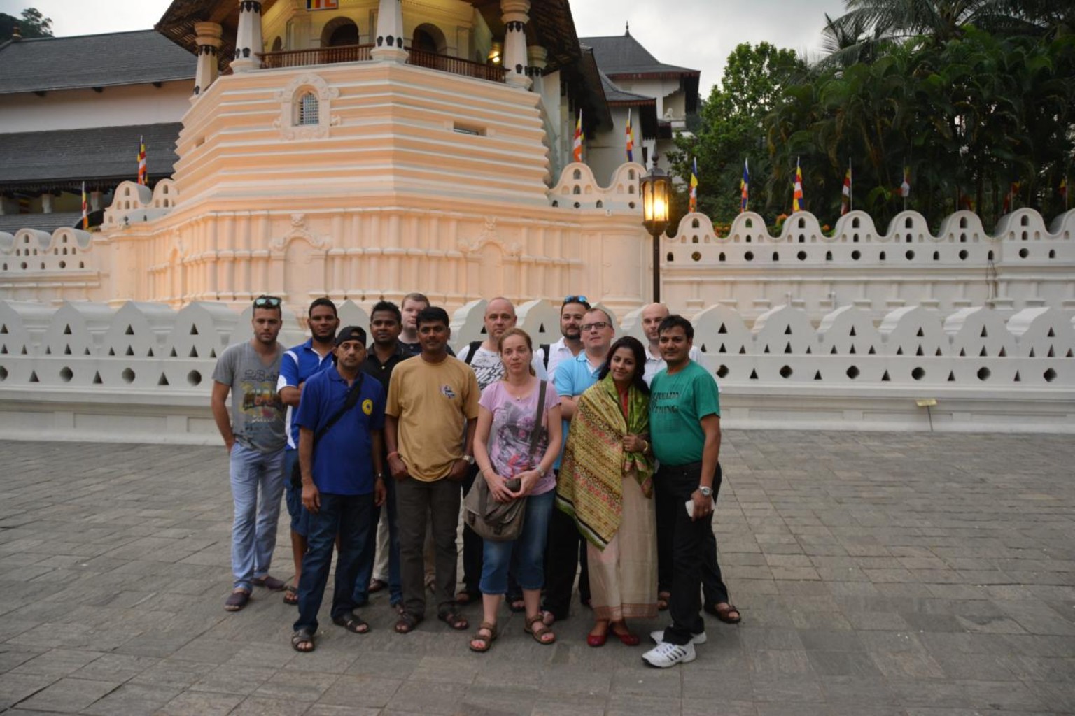 A mixed group of men and women gathered in front of a temple's white wall and ornate entrance