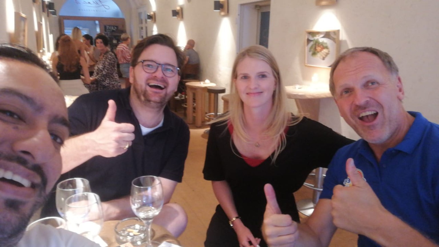 Friends, men and a woman, smiling and giving thumbs-up around a restaurant table