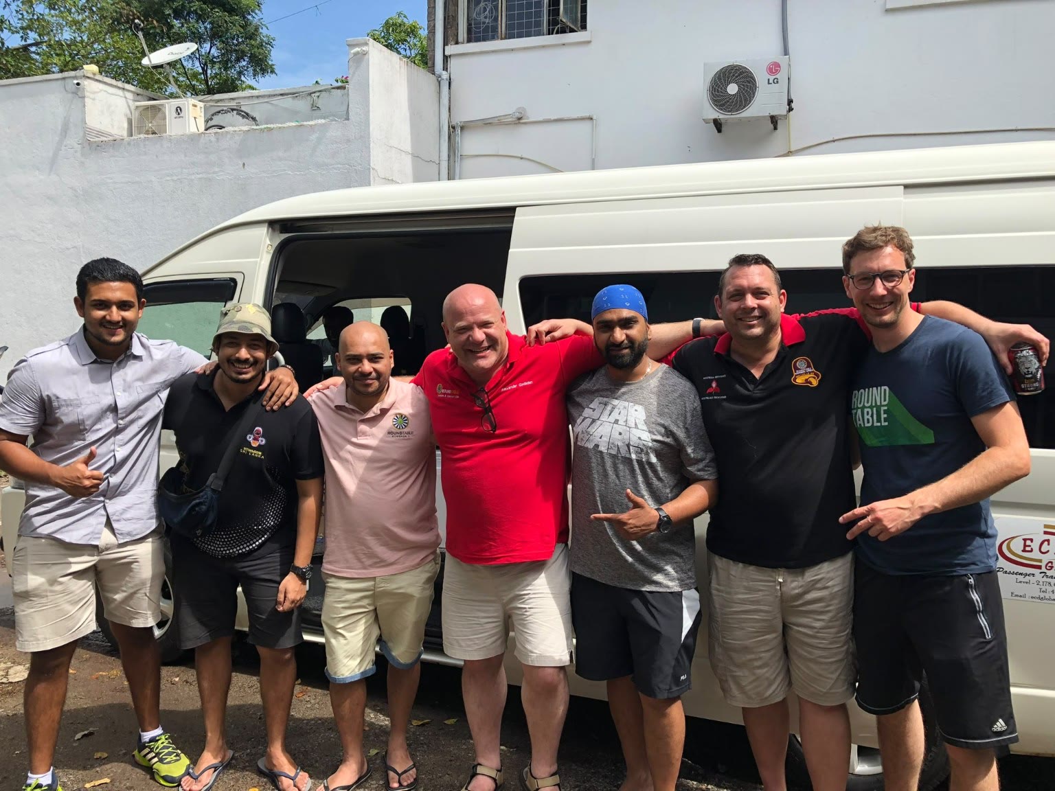Seven friends in Round Table shirts beside a white minivan